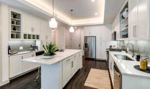 Modern kitchen with white cabinetry, marble island, and stainless steel appliances, lit by pendant lights over dark hardwood floors.